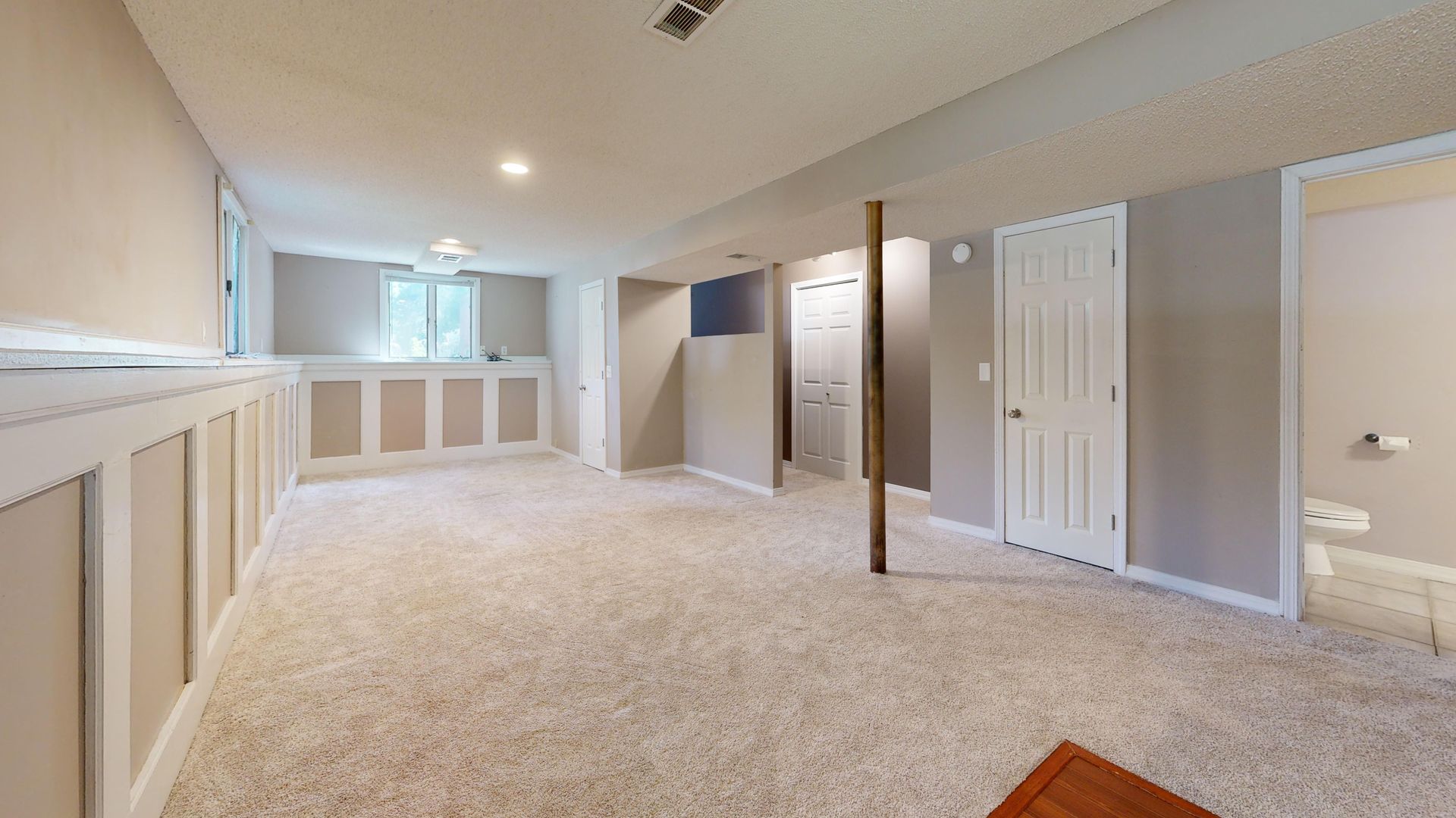Bright and clean modern basement with carpet flooring and recessed lighting.