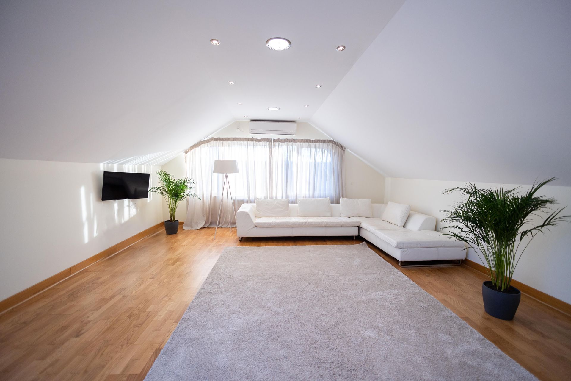 Spacious attic living room with white sofa, hardwood floor, and modern decor.